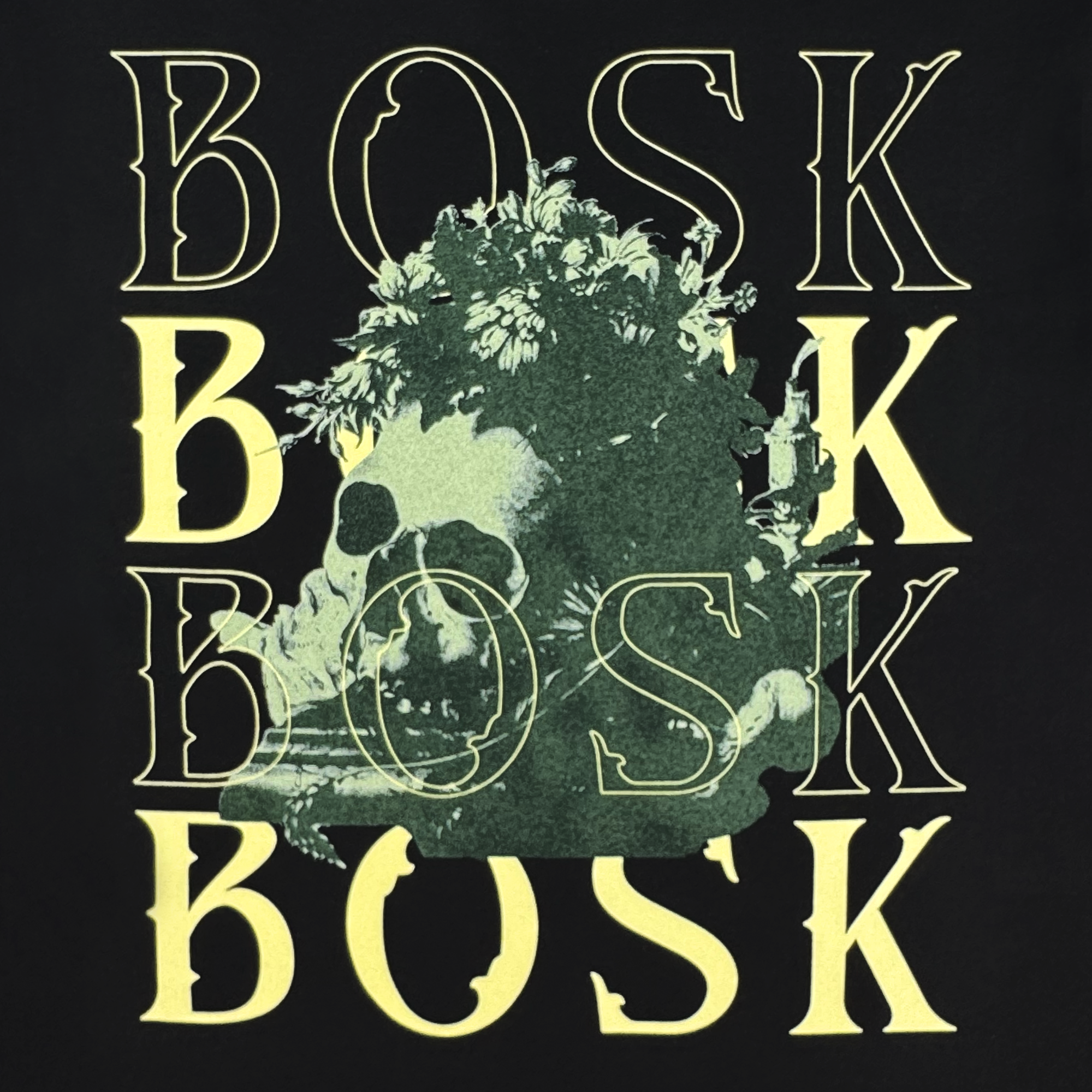 The Allure LS Tee by BOSK features "BOSK" repeated four times in pale yellow over black, with a greenish skull amid foliage at the center—a striking design on this 100% cotton long sleeve t-shirt.