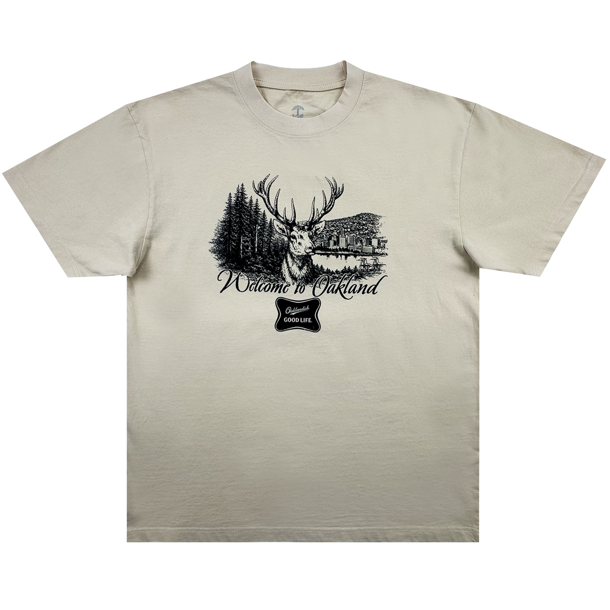 The Buck Tee by Oaklandish is a beige men’s t-shirt with a black stag, pine trees, and lake cabin graphic. Made from heavy-weight cotton, it features "Welcome to Oakland" in cursive and a “good life” badge below.