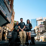 Two women and a man standing in front of a lowrider car in Oakland wearing Oaklandish t-shirts.
