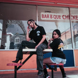 Two women sitting outside an Oakland BBQ restaurant wearing Oakland Crusin graphic tees.