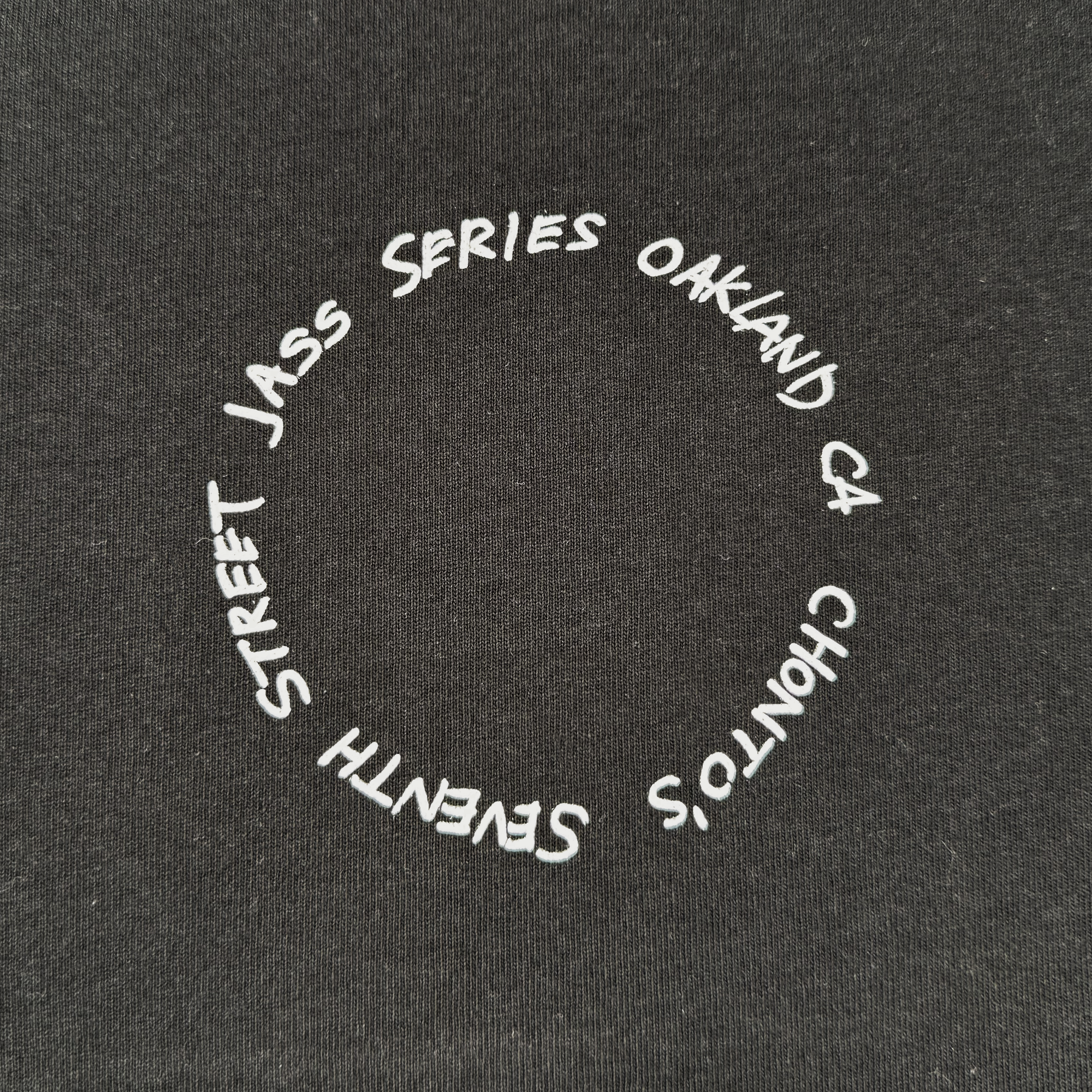 The Ode to Jass Tee by Oaklandish features white, handwritten-style text in a loose circle on black, reading "OAKLAND CA, CHONTO’S, SEVENTH STREET JASS SERIES." This classic fit tee is made from 100% cotton for comfy, artistic everyday style.