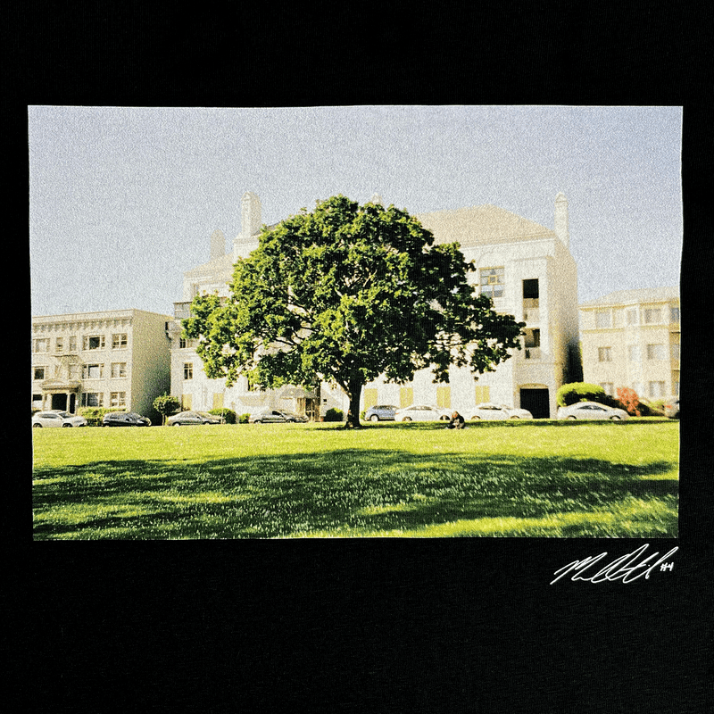 Close-up of signed photographic image of a tree with a building behind on a black t-shirt.