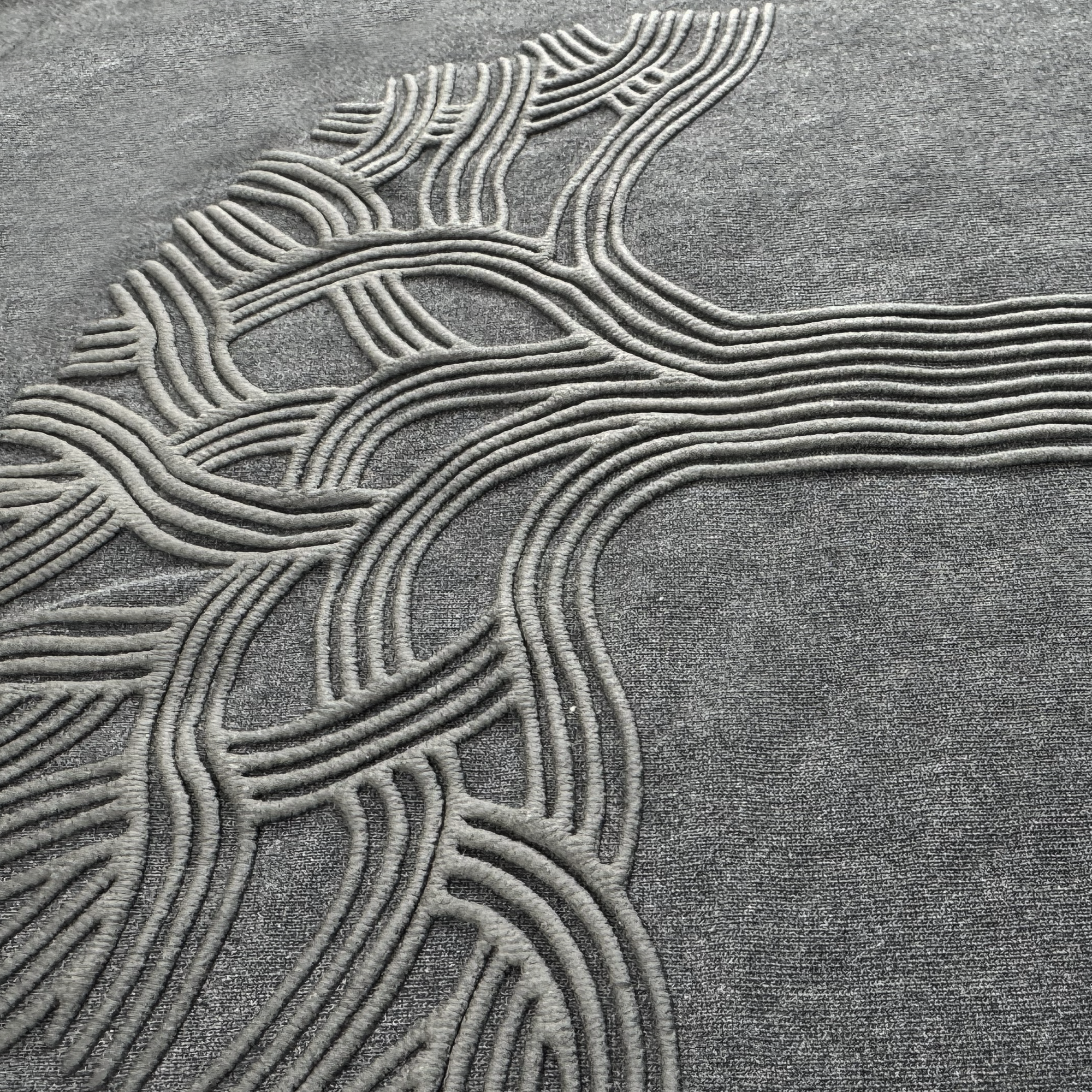 A textured gray carpet features a raised, abstract pattern reminiscent of intertwined tree branches, creating a three-dimensional effect similar to the distinctive design on the Oaklandish Classic Logo Tee by Oaklandish.