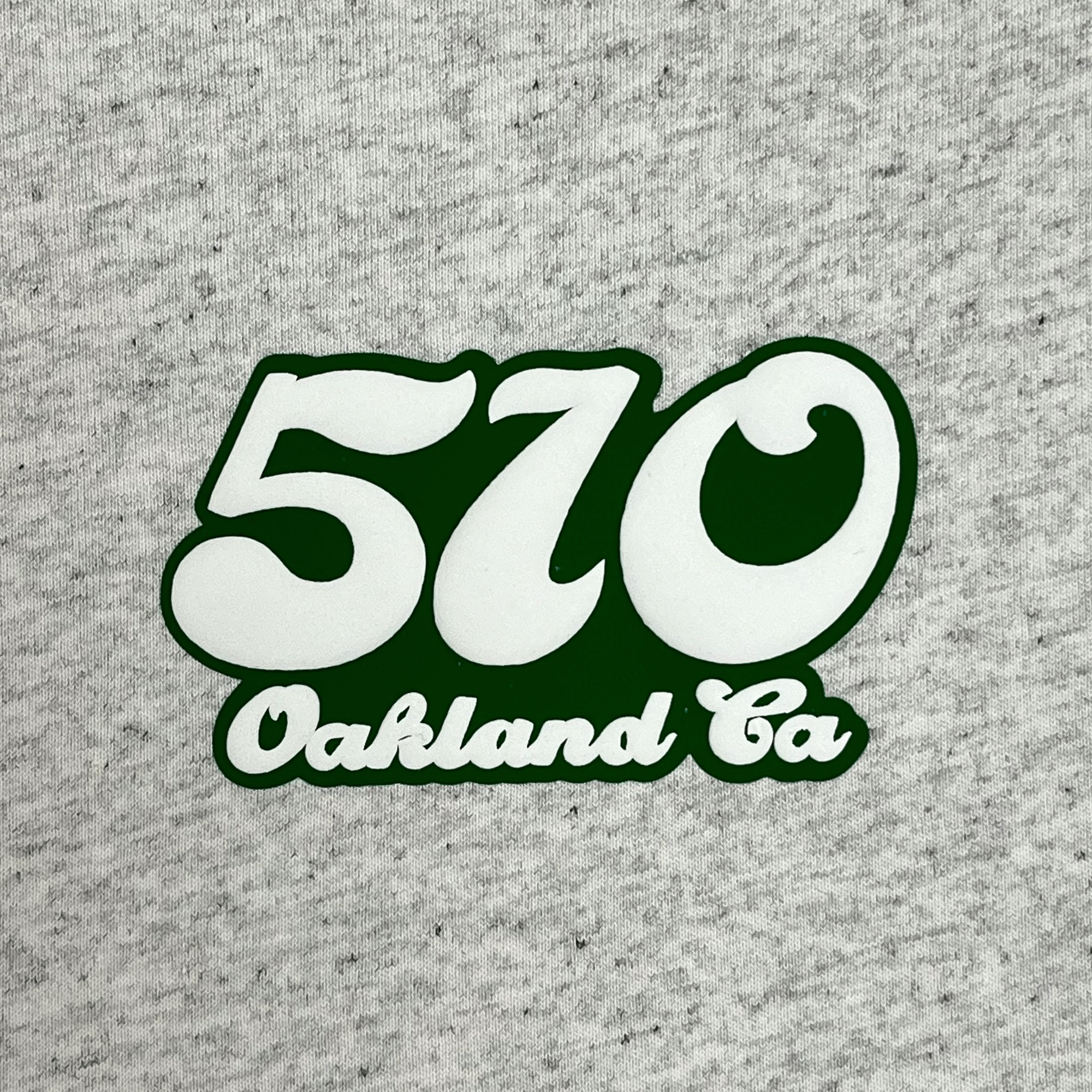 Close-up of puff 510 Oakland CA graphic on left chest wearside on heather grey t-shirt.
