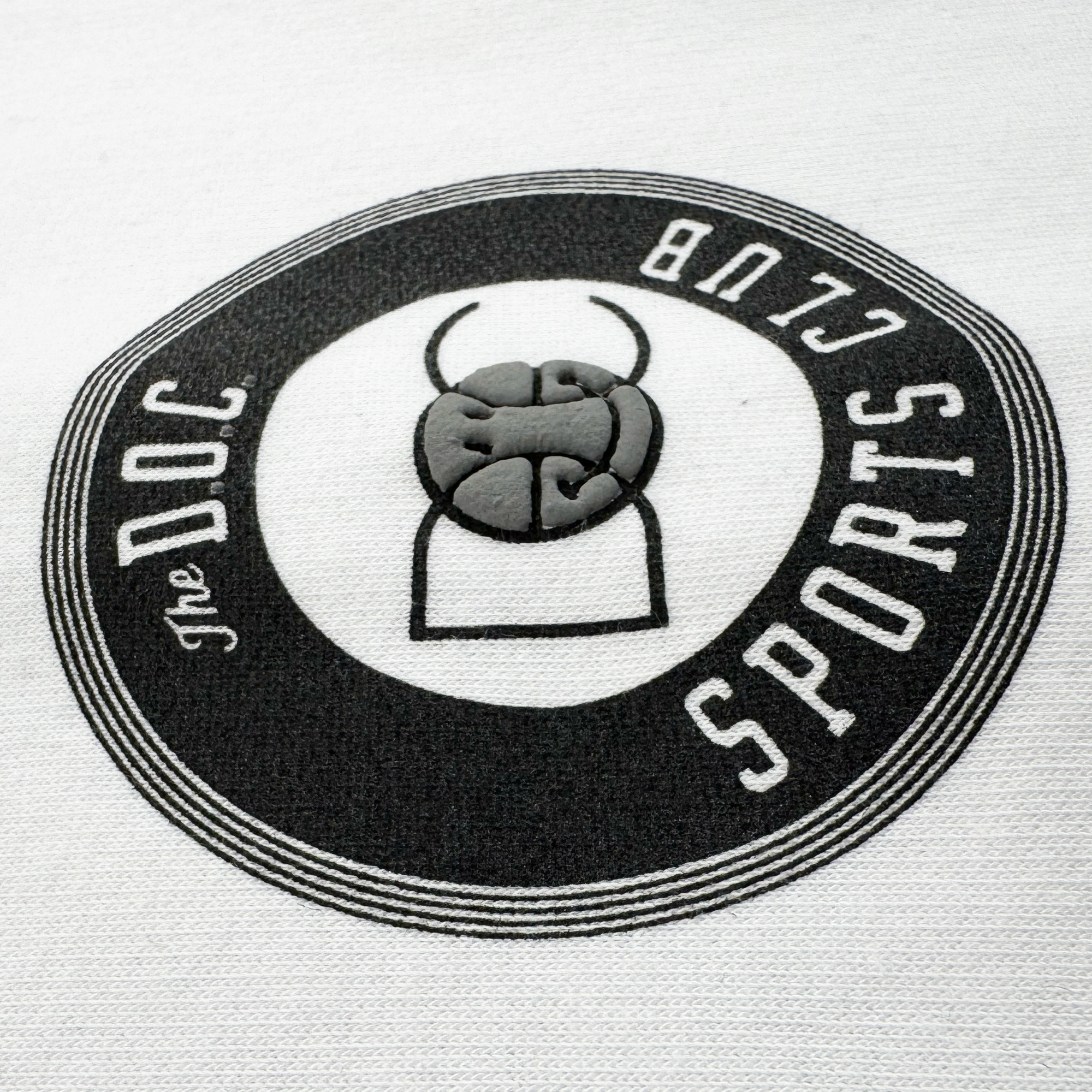 A circular black-and-white logo with “THE DOC SPORTS CLUB” accents this Bay Bridge Hoodie By DOC V2 from Oaklandish, featuring a stylized fist and rectangle printed on a white fleece pullover.