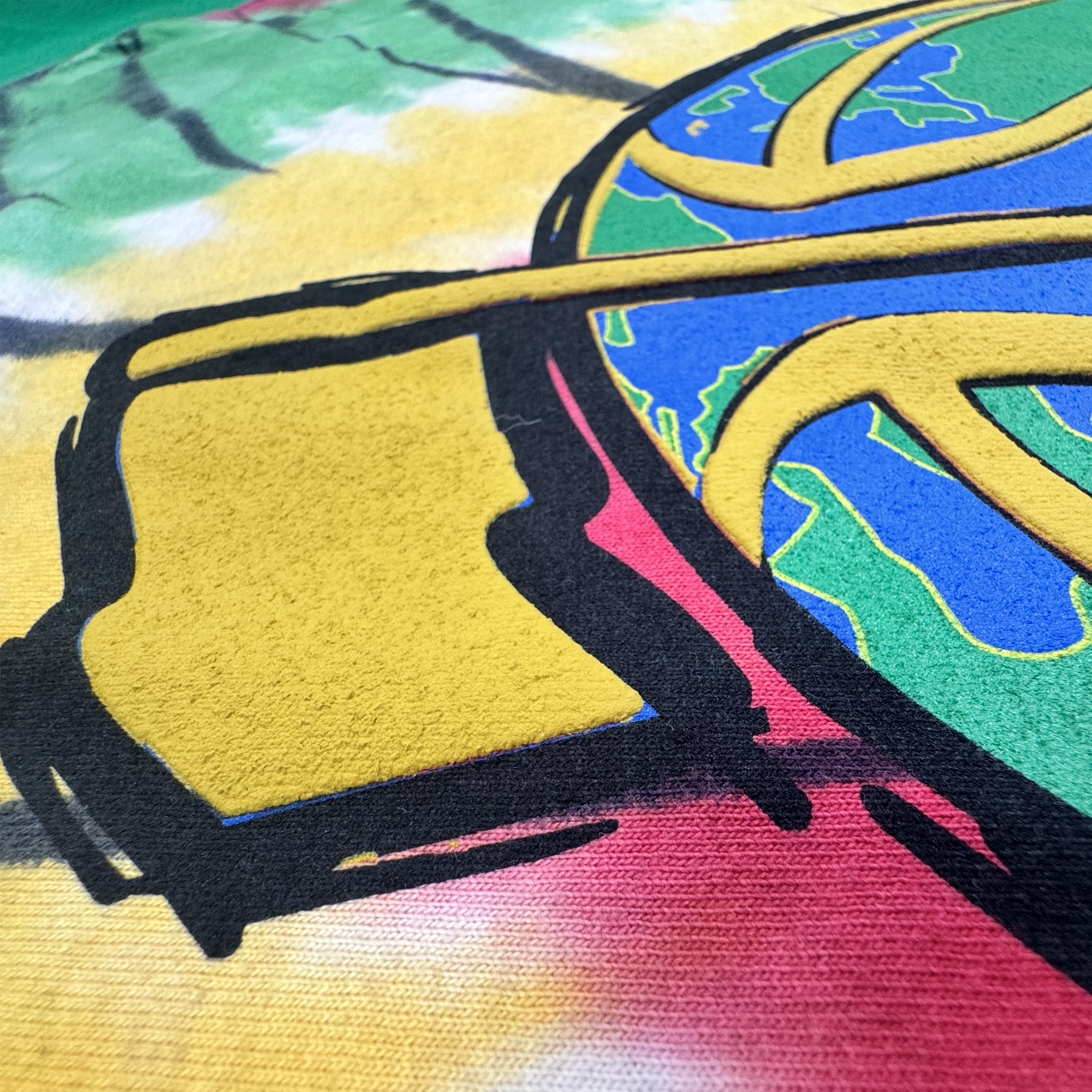 A close-up of colorful street art featuring bold black outlines, a yellow square, and a partial globe with visible continents, set against a background blending green, yellow, and red hues with a textured canvas surface—reminiscent of the vibrant patterns found on The Dead Golf Tee By Doc by By DOC, crafted from heavyweight cotton in a classic fit.