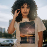 Female model wearing graphic t-shirt with photo of lightning over Bay Bridge in Oakland on natural cotton colored t-shirt.