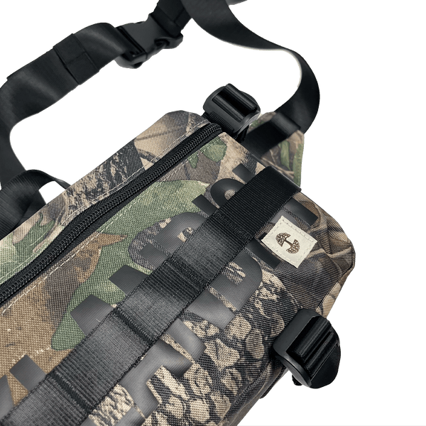 Top side view of a camo pattern cross-body bag with front zipper and large black Oakladish wordmark and Oaklandish tree logo patch.