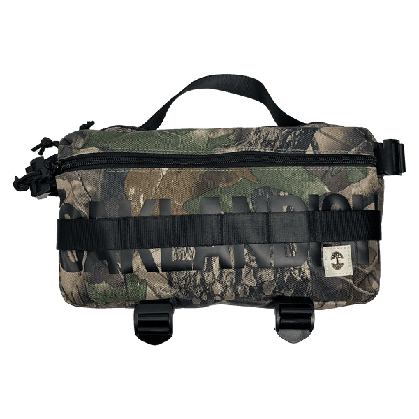 Front view of a camo pattern cross-body bag with front zipper and large black Oakladish wordmark and logo patch.