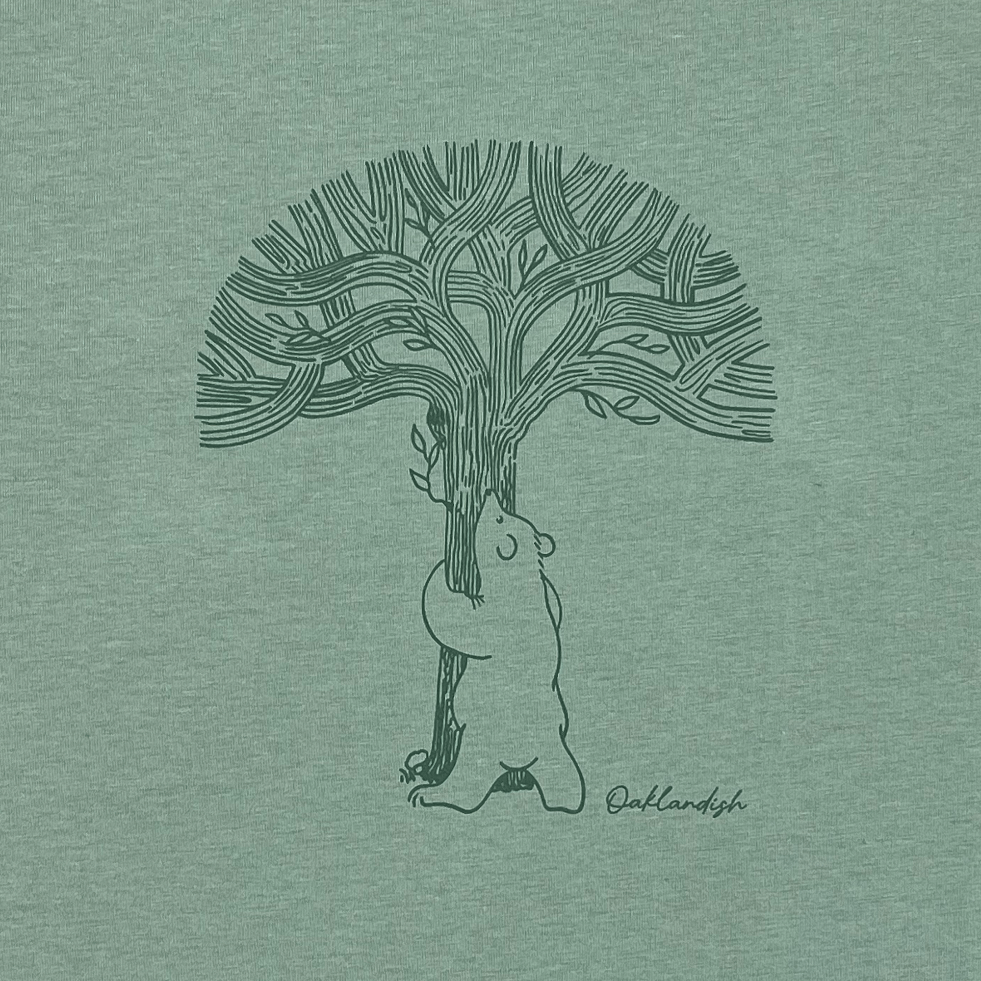 Close-up of line graphic featuring a bear hugging a tree representing Oaklandish with Oaklandish wordmark on sage green women’s cut t-shirt.