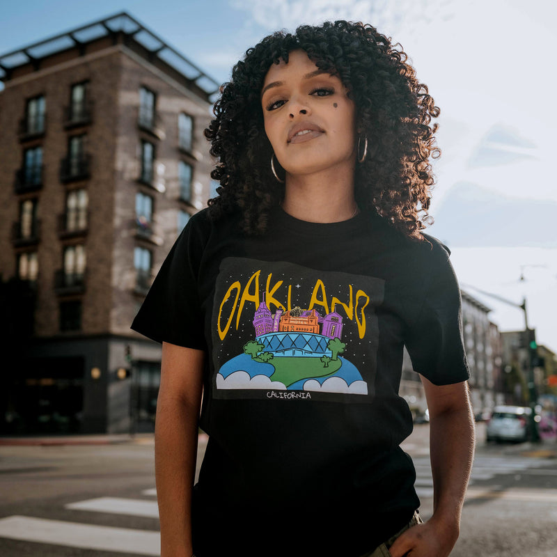 Female model wearing black cotton t-shirt with  graphic depicting Oakland places depicted as full-color celestial spaces .