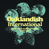 Close-up of green and yellow Oakland International graphic with a caption celebrating global diversity since 2000 on a black tee. 