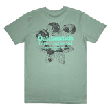 Backside of a sage green t-shirt featuring a green and yellow Oakland International graphic with a caption celebrating global diversity since 2000. 