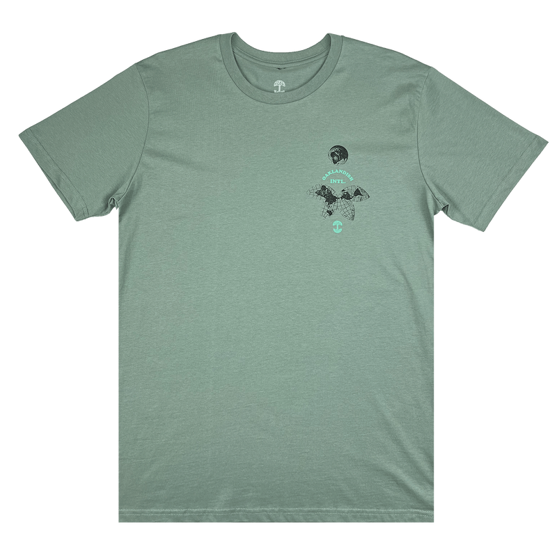 The front side of a sage green t-shirt with a small Oakland International graphic and Oaklandish tree logo on the upper chest.