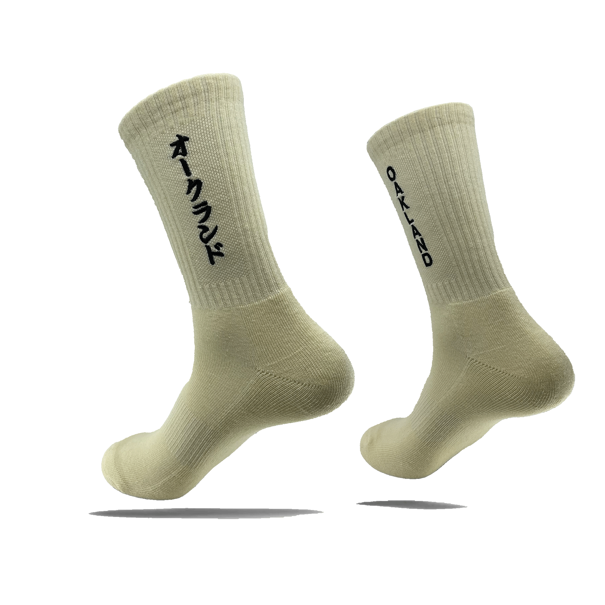 Side view of a pair of white crew socks with a black embroidered OAKLAND wordmark on the side of one sock and Kanji Japanese writing on the other.
