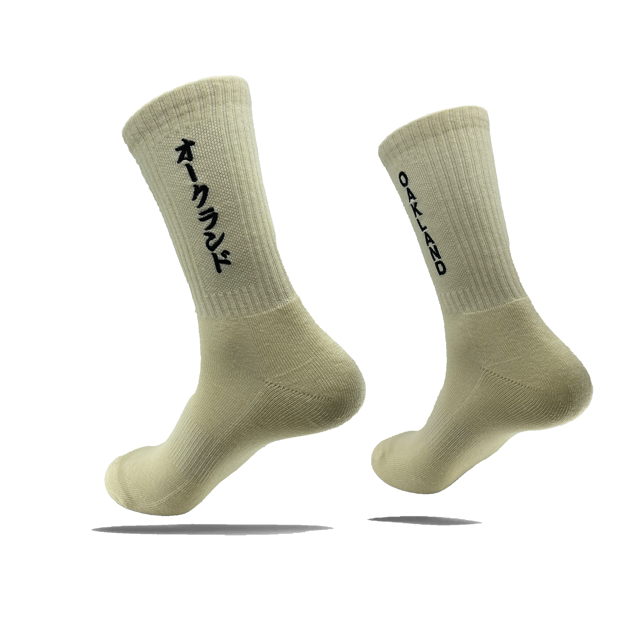 Image of the "Kanji Sock" by Oaklandish, a pair of off-white, ribbed ankle socks. The left sock displays Japanese Katakana characters in black, while the right sock features the word "OAKLAND" in black capital letters. Both cotton socks are shown against a plain white background, slightly elevated to showcase their design. Available in adult sizes.