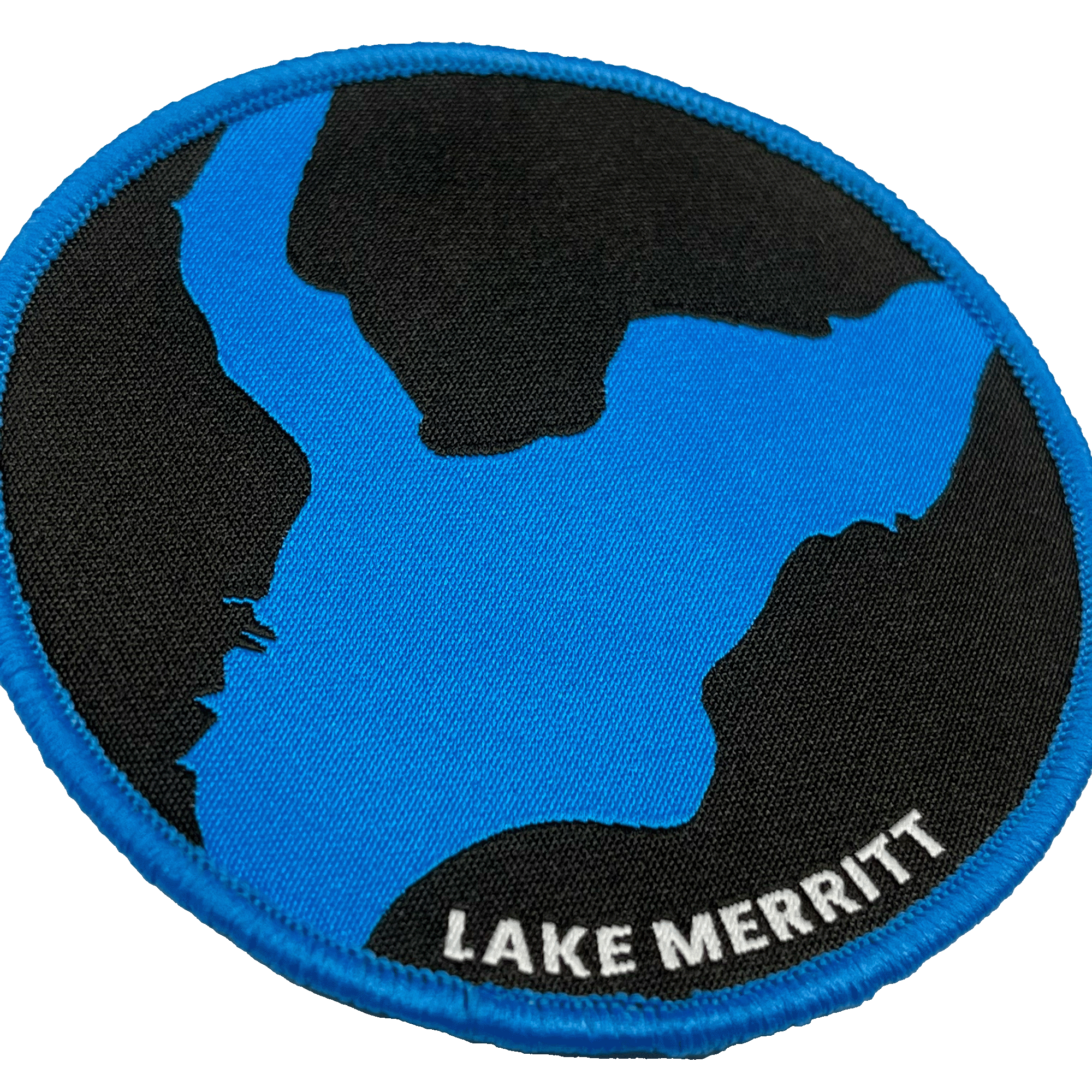Close-up of black woven iron-on patch with a blue outline of Oakland's Lake Merritt & Lake Merritt wordmark.