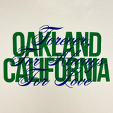 Close-up of OAKLAND CALIFORNIA wordmark in green with a blue Forever. For Always. For Love in script on a natural cotton color t-shirt.