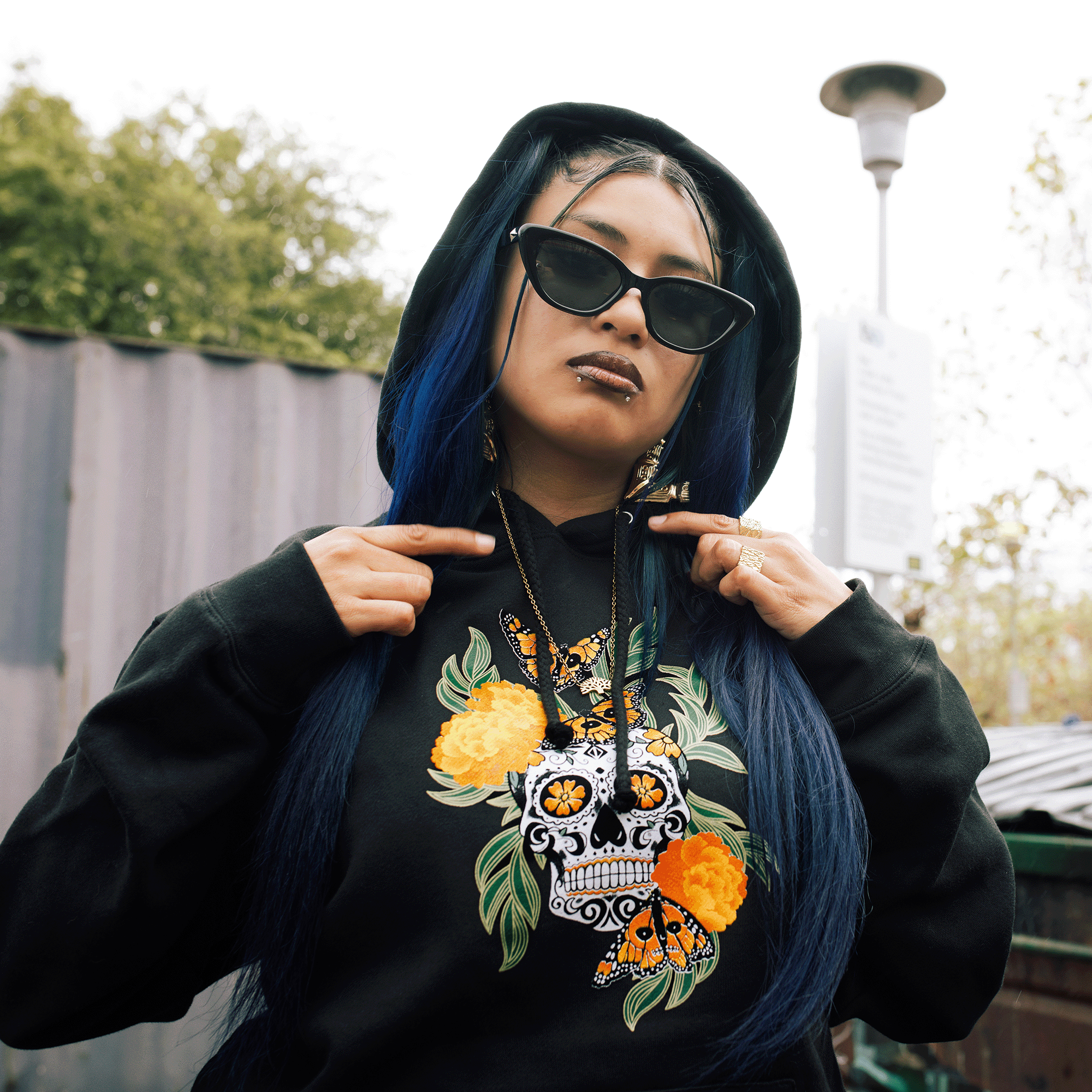 Detailed photo of female model wearing black pullover hoodie with graphic art by Oakland artist Jet Martinez depicting a sugar skull surrounded by Marigolds and Monarch butterflies.
