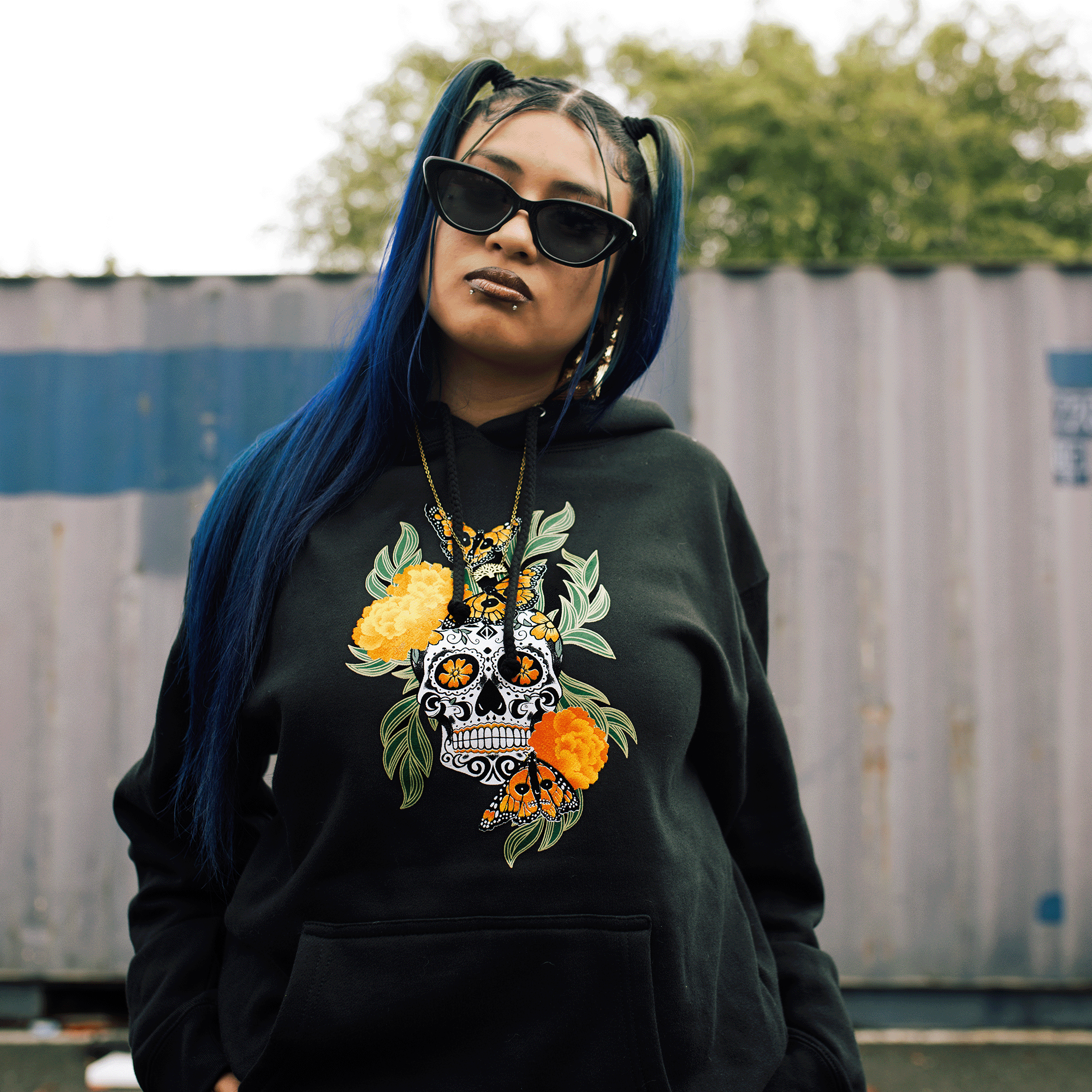 Female model wearing black pullover hoodie with graphic art by Oakland artist Jet Martinez depicting a sugar skull surrounded by Marigolds and Monarch butterflies.