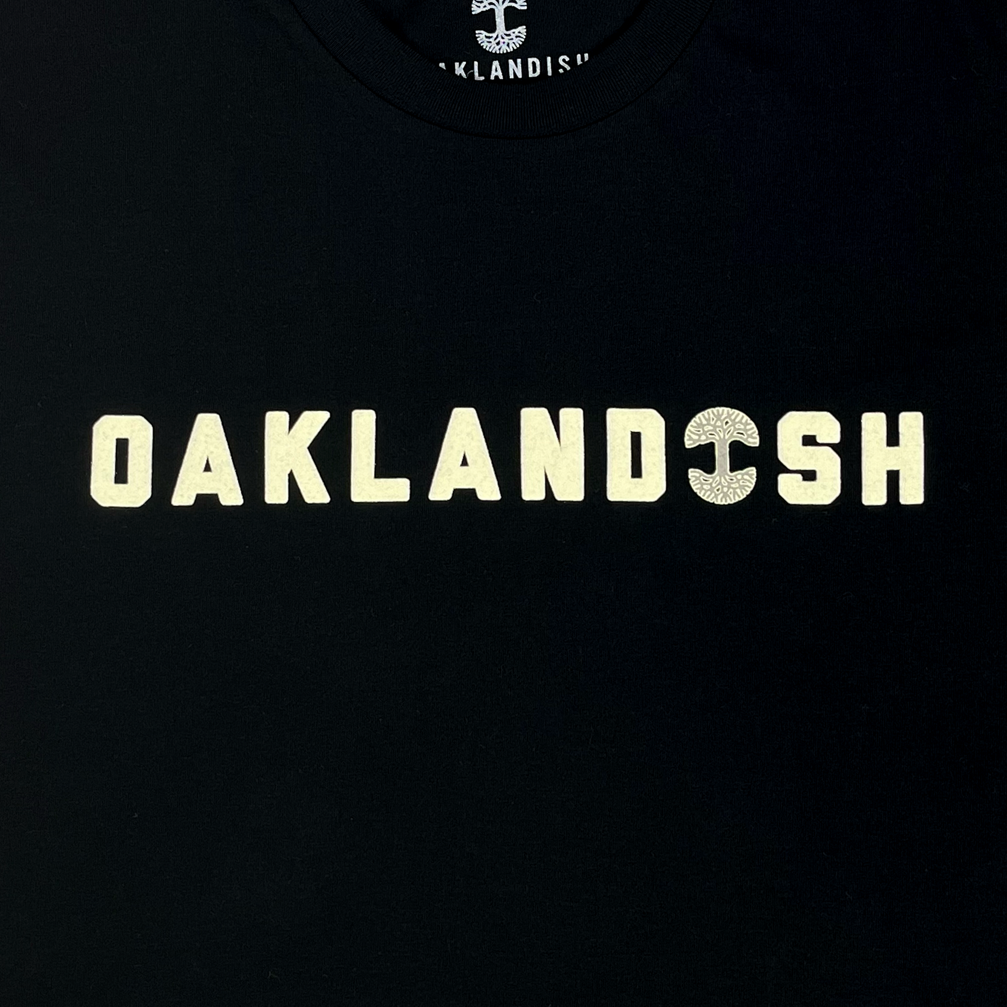 Detailed view of Cotton black t-shirt with Oaklandish Wordmark and Oaklandish tree logo in place of 'i'.