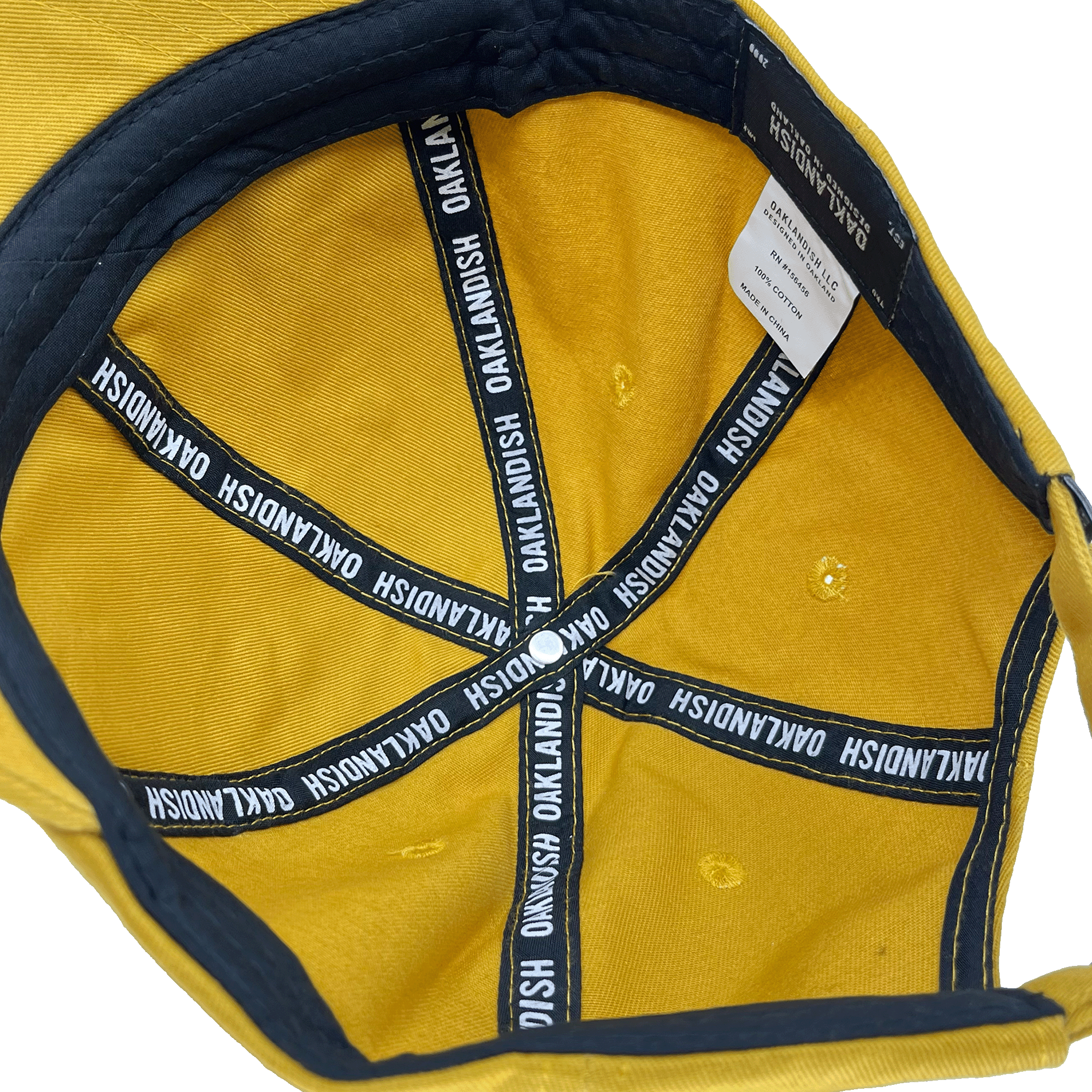 Inside crown view of the black striping inside a mustard yellow dad cap with a white Oaklandish wordmark on repeat.