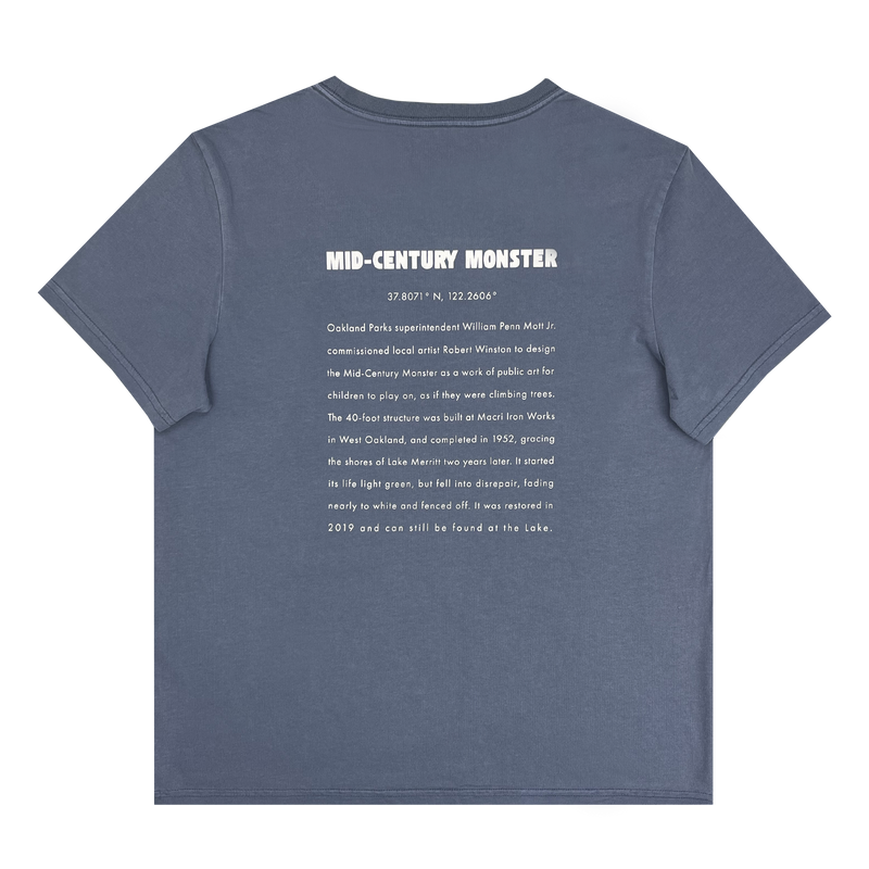 The backside of a faded blue women’s t-shirt with long-form text explaining the history of the mid-century monster structure at Oaklands Marci Iron Works.