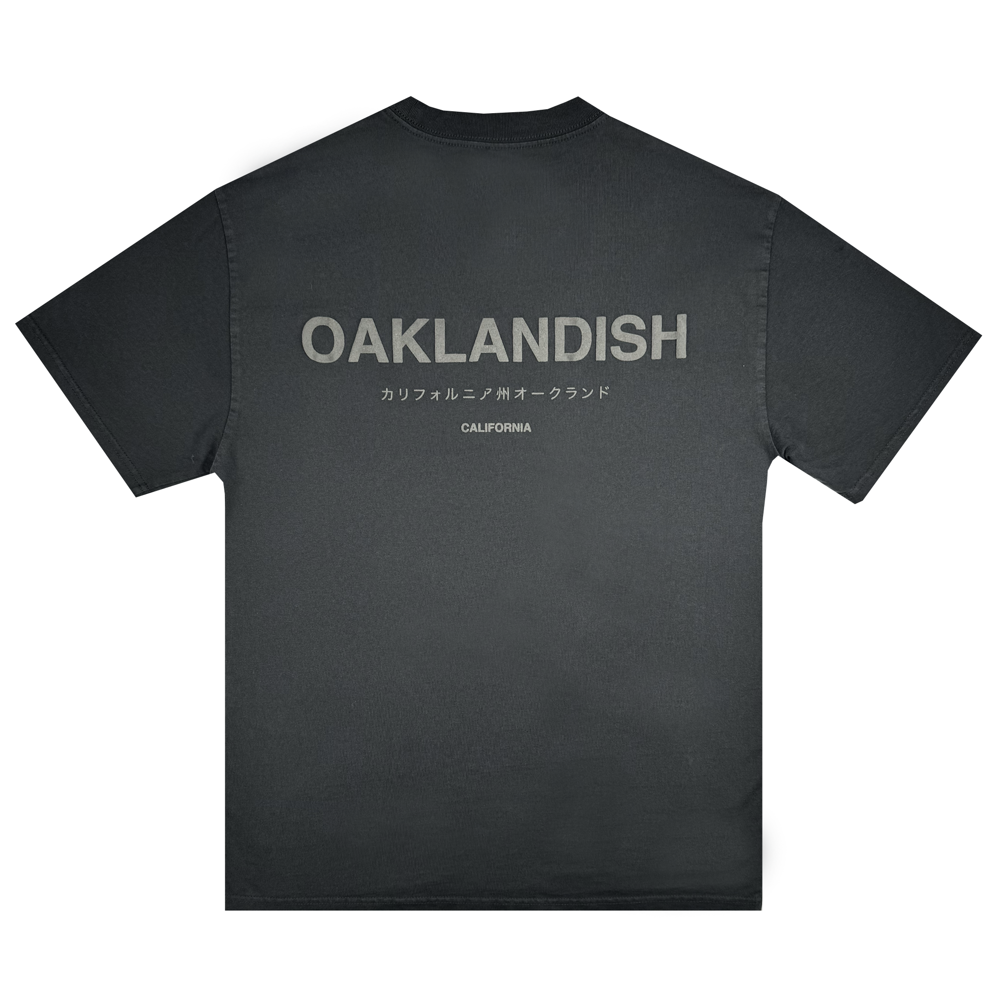 The Modern Type Heavy Tee by Oaklandish, made from heavyweight cotton in a faded black shade, showcases bold gray "OAKLANDISH" lettering across the back. Below it, the word "CALIFORNIA" appears in smaller gray font alongside Japanese text. The shirt is displayed against a plain white background.