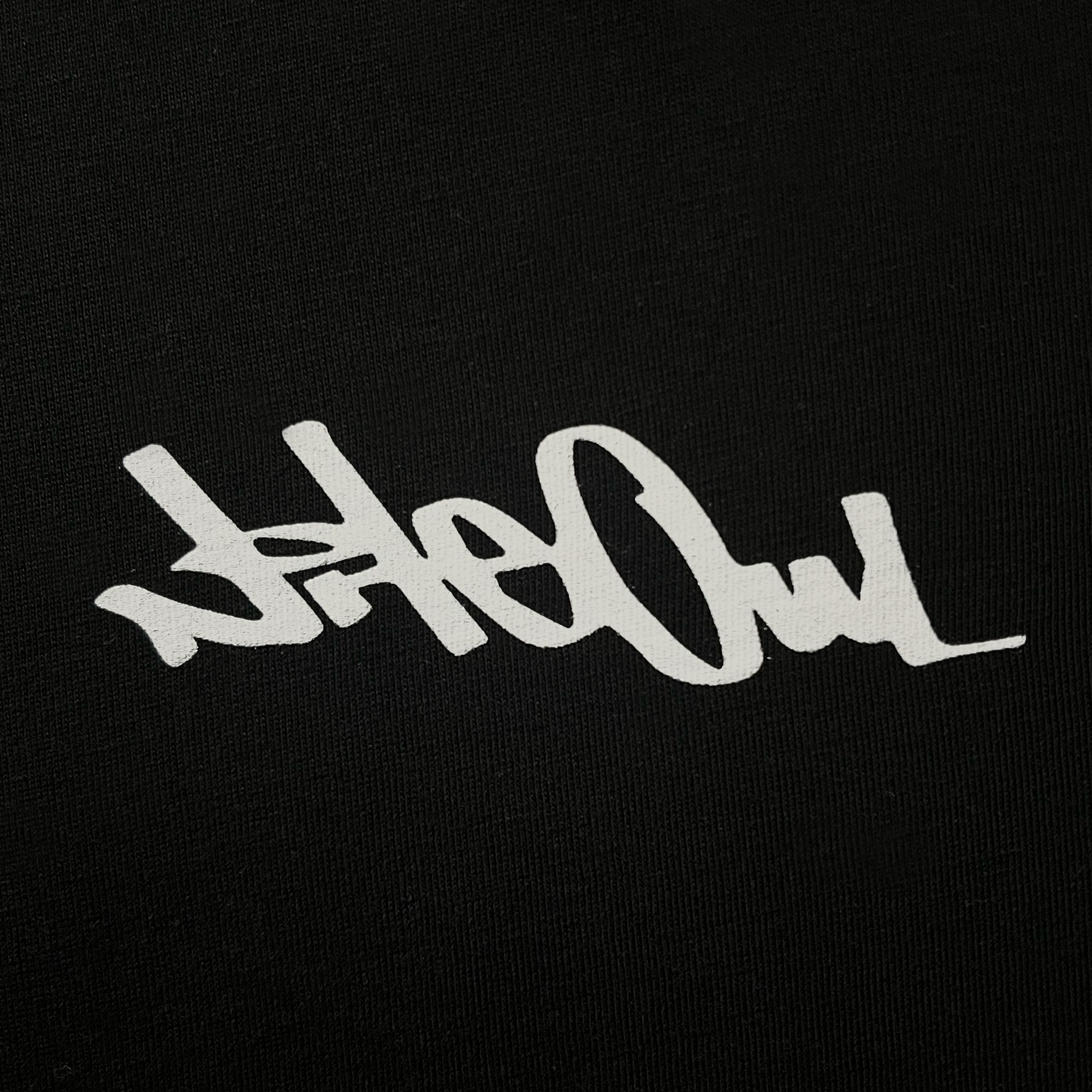 Front close-up of Oakland artist Nite Owl logo/signature in white ink on the chest of a black t-shirt.