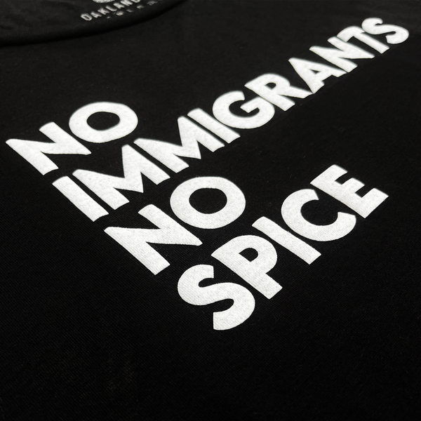 Detailed close-up of NO IMMIGRANTS NO SPICE wordmark on the front chest of a women’s black cotton tank top.