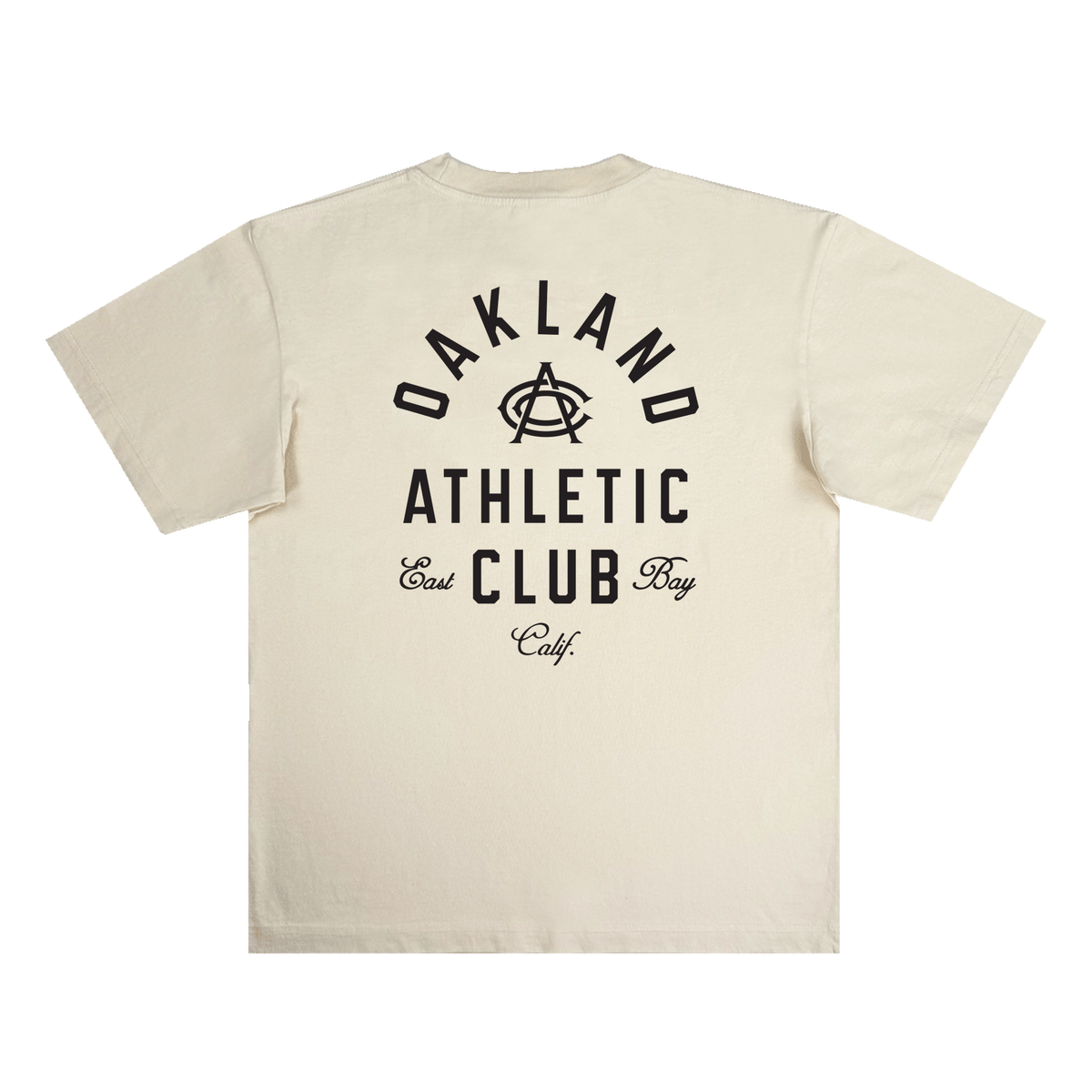 The OAC Tee by OAC is a cream-colored, classic fit t-shirt made from heavy-weight cotton. It features bold black text on the back that reads “OAKLAND ATHLETIC CLUB East Bay Calif.” with a stylized interlocking “A” and “C” at the center. The shirt is displayed flat against a white background.