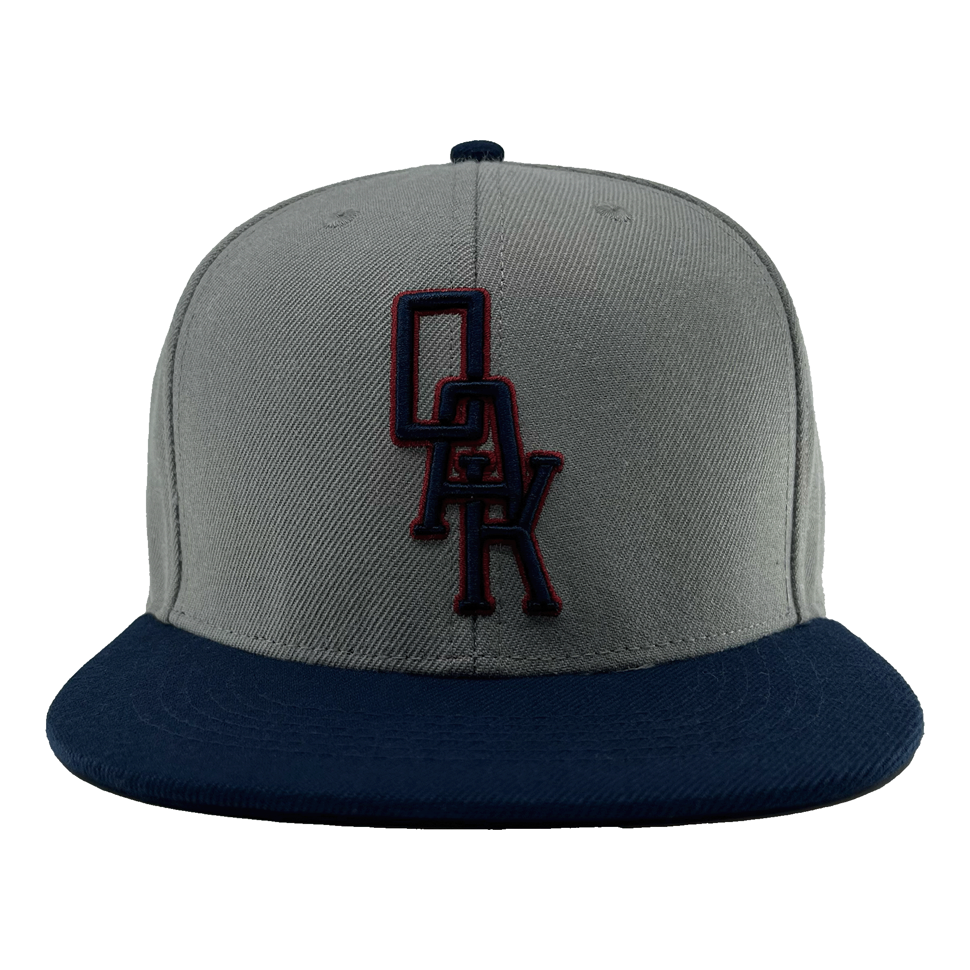 A close-up image of the OAK Monogram Snapback by Oaklandish, showcasing its grey body and navy blue brim. Embroidered in navy blue and outlined in red on the front panel is the distinctive "OAK" logo, evoking Oaklandish style. The cap is centered against a plain green background.