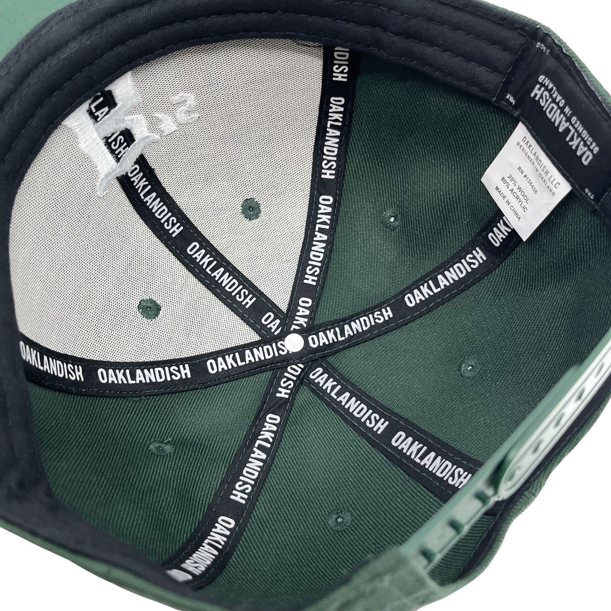 Inside crown view of a forest green cap with black striping with Oaklandish wordmark on repeat.