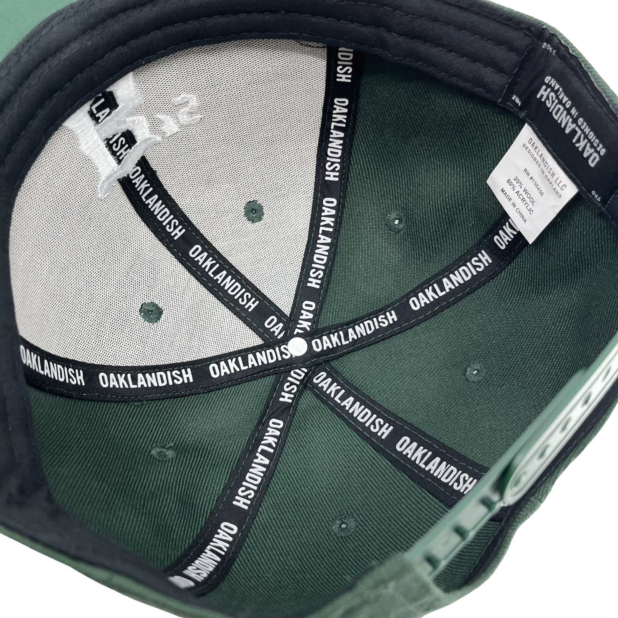 Interior view of the Oakland Ballers Snapback. The inside features black seams repeatedly labeled "OAKLANDISH" in white text. The label inside includes washing instructions and material information. The cap also has a small logo design on the inner top panel, celebrating the Oakland Ballers, a Pioneer League professional baseball team. The brim is lined with black fabric.