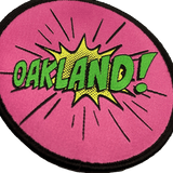 Close-up of embroidered iron-on patch with Oakland wordmark in comic cartoon punch style in pink, green and yellow.