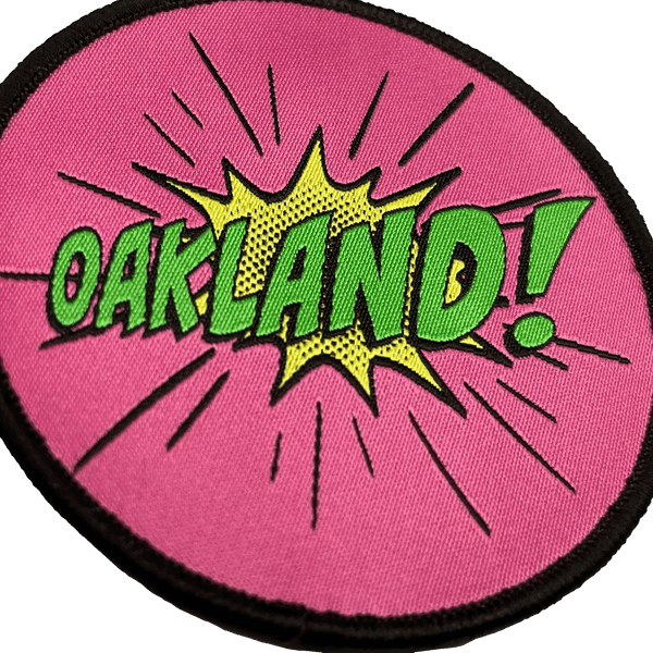 Close-up of embroidered iron-on patch with Oakland wordmark in comic cartoon punch style in pink, green and yellow.