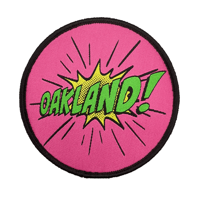 Embroidered iron-on patch with Oakland wordmark in comic cartoon punch style in pink, green and yellow.