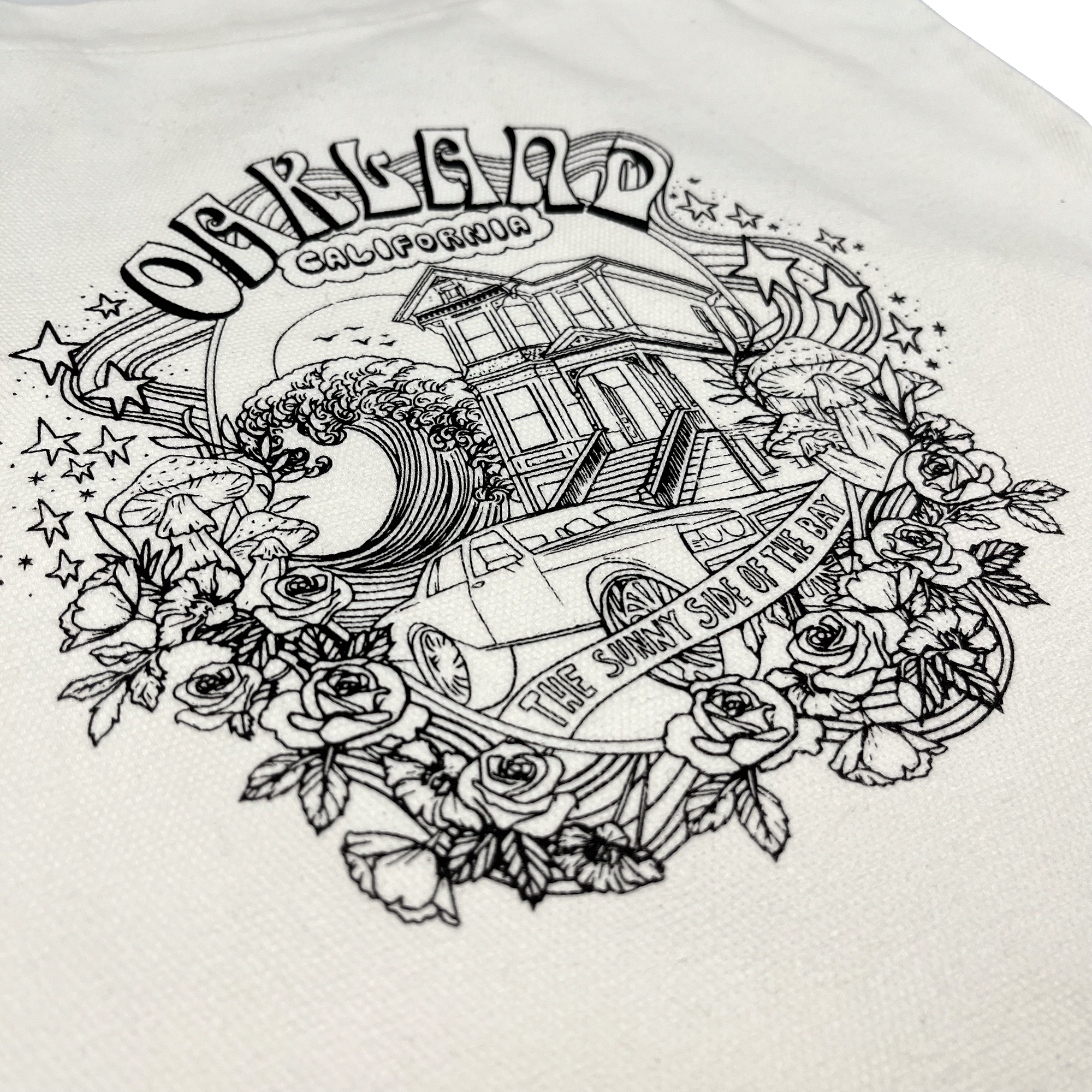 The Oakland Dream Tote by Oaklandish showcases a black and white illustration on a cotton tote bag, portraying Oakland, California. The design features a house, a car, and a large wave surrounded by flowers, stars, and a ribbon with the text "The Sunny Side of the Bay." The word "Oakland" is prominently displayed at the top of this stylish accessory.