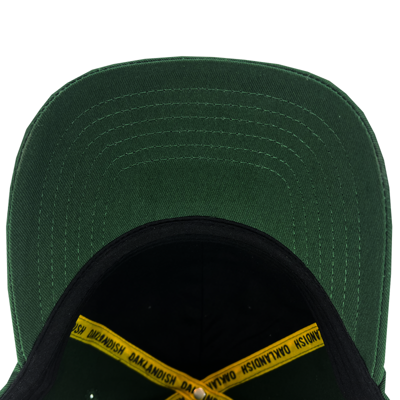 View the underside of the forest green dad cap visor and inside the crown with yellow taping with ‘OAKLANDISH' wordmark on repeat.