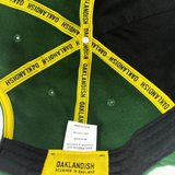 Inside crown of forest green dad hat with yellow taping with Oaklandish wordmark on repeat and Oaklandish patch.