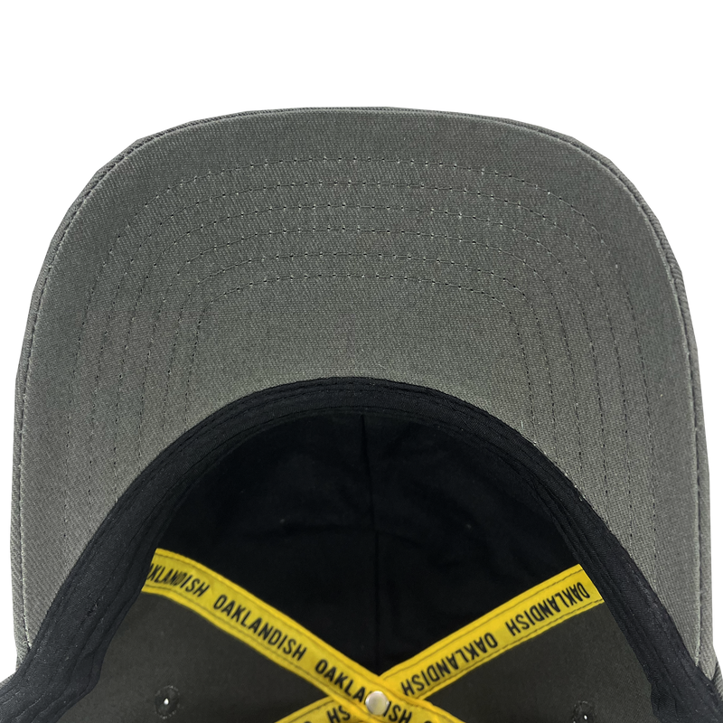 Inside crown of dark grey dad hat with yellow taping with Oaklandish wordmark on repeat and Oaklandish patch.