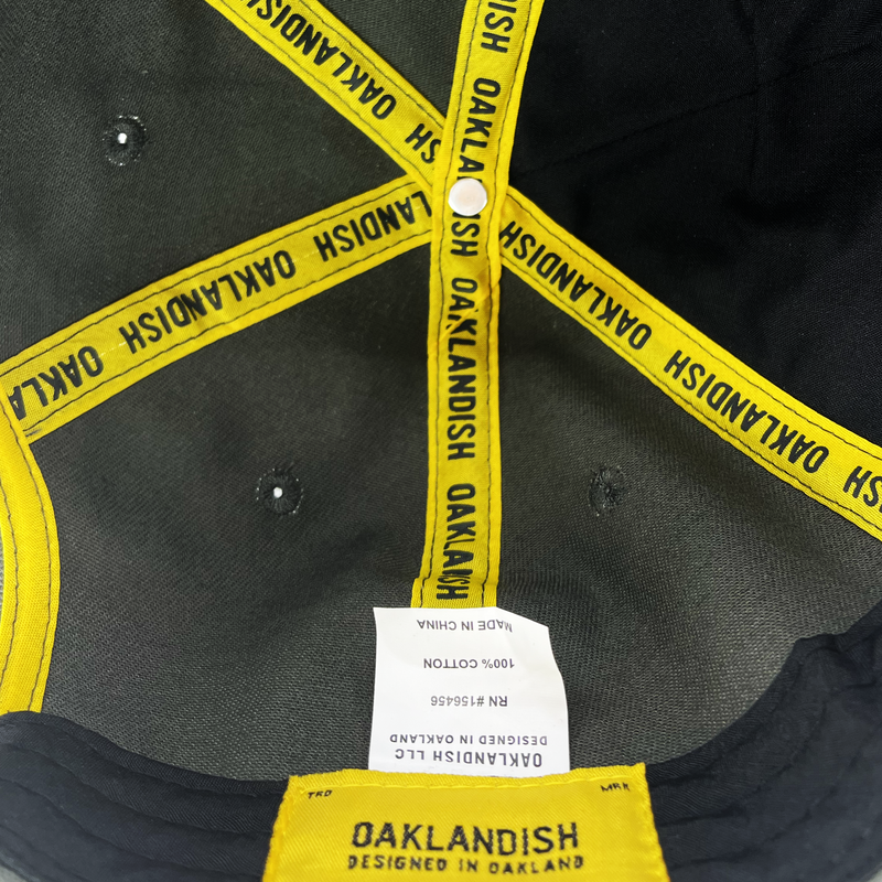 Close up inside crown of dark grey dad hat with yellow taping with Oaklandish wordmark on repeat and Oaklandish patch.