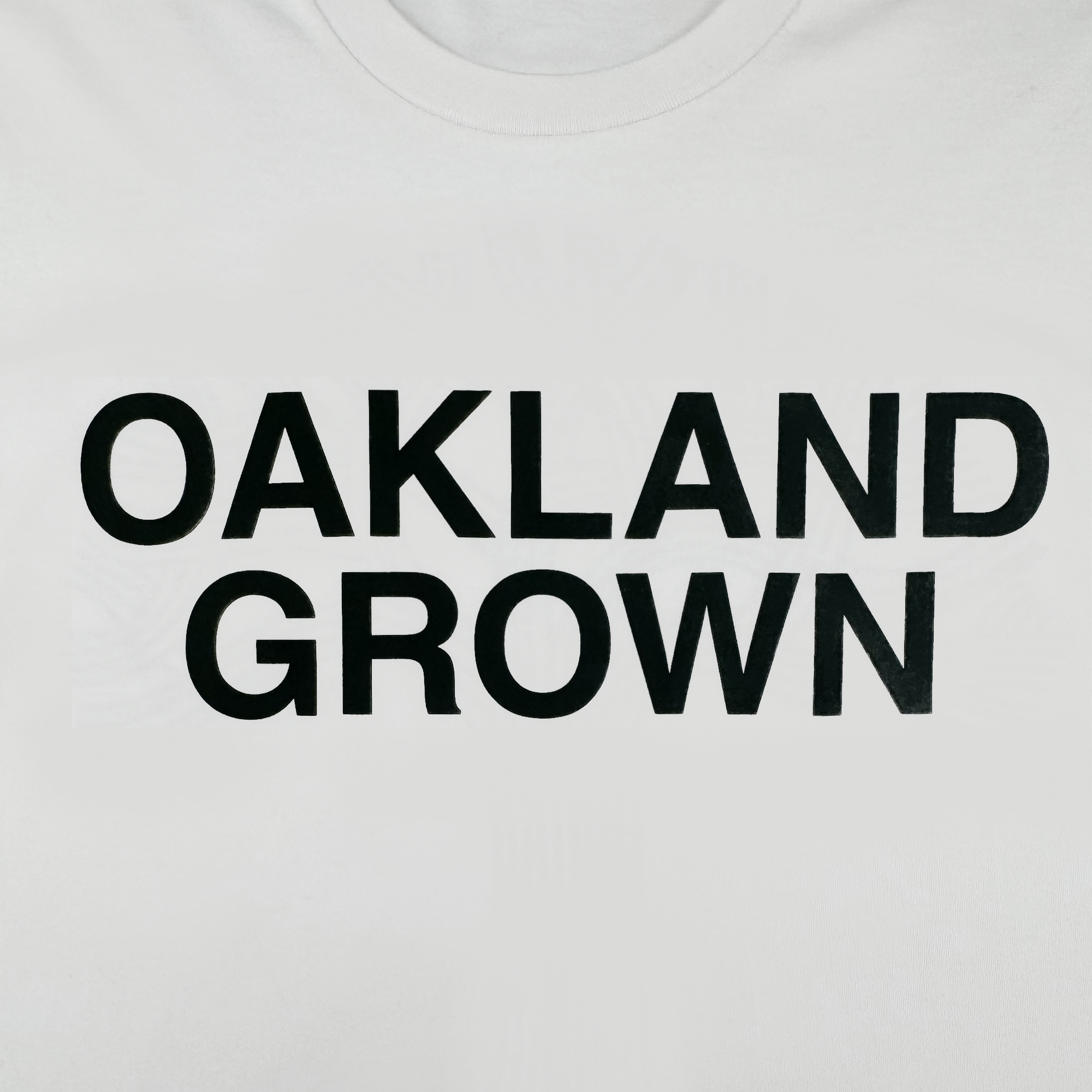 The Oaklandish Oakland Grown Tee is a white, 100% cotton men’s classic fit t-shirt featuring bold, black “OAKLAND GROWN” text printed across the front.