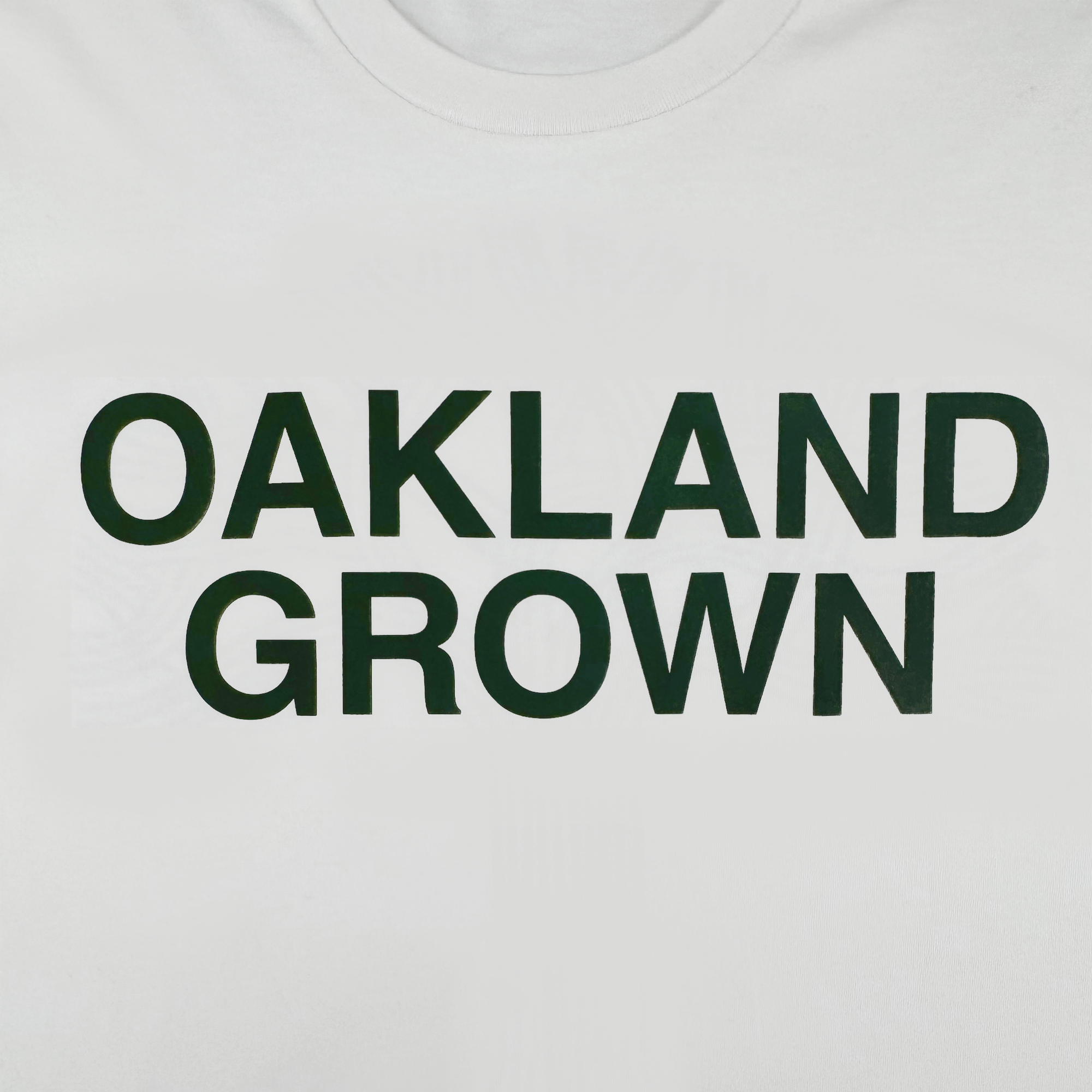 The Oaklandish Oakland Grown Tee is a classic white men’s t-shirt made from 100% cotton, featuring “OAKLAND GROWN” in bold black capitals centered on the front with no other graphics.