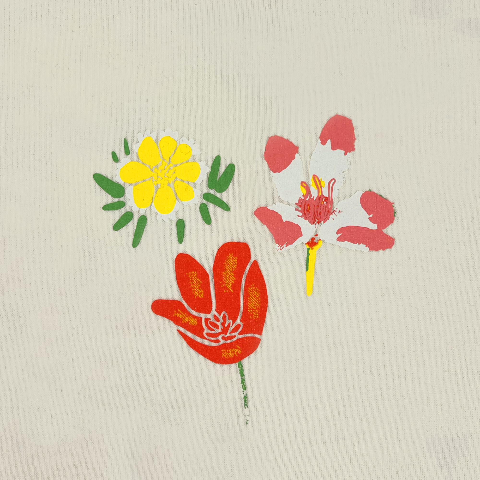 Close-up of a small graphic of 3 Oakland Wildflowers on the left chest of a natural cotton-colored t-shirt.