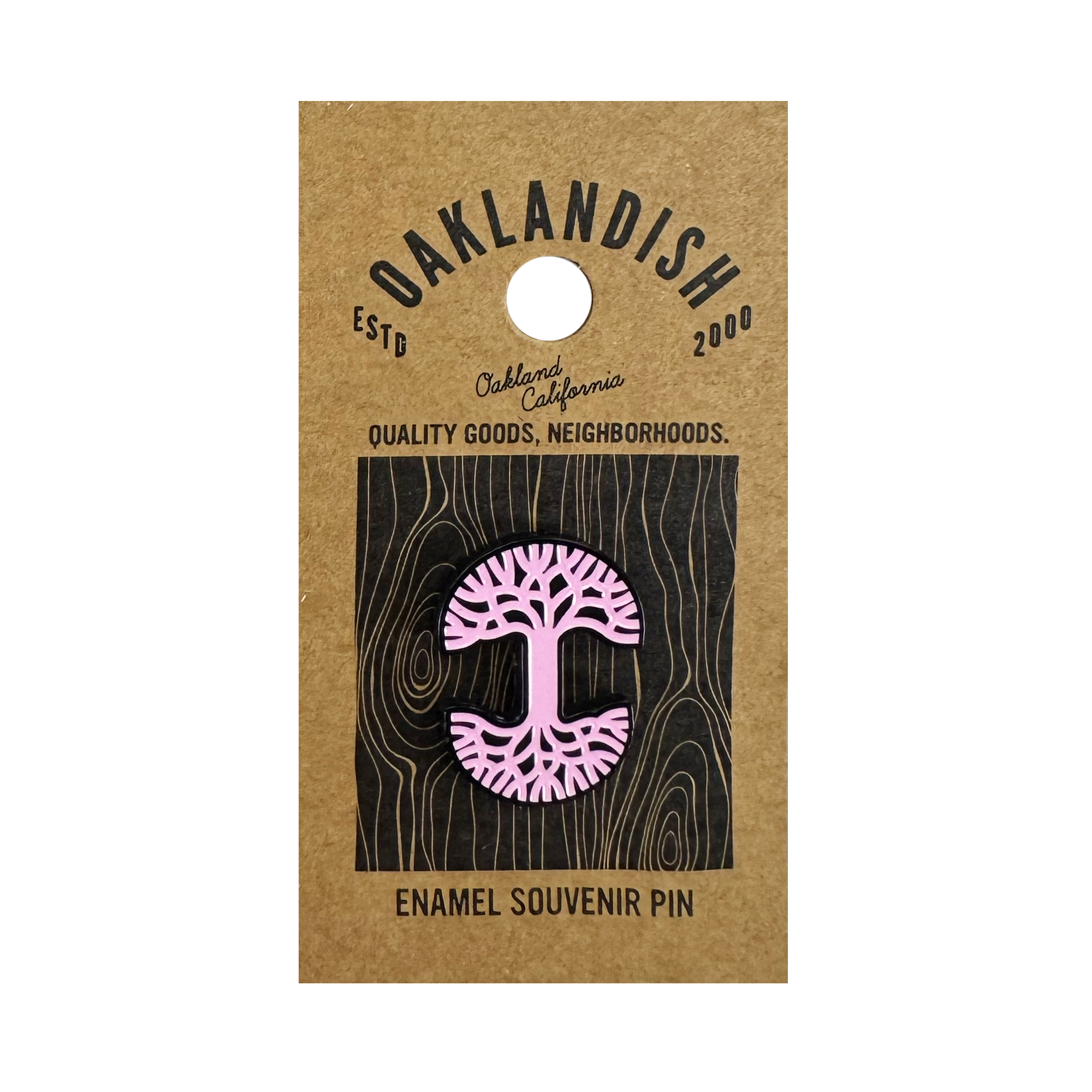 The Oaklandish Logo Enamel Pin is a pink enamel accessory shaped like a stylized tree with exposed roots, attached to a brown Oaklandish card labeled “Oakland, California,” “ESTD 2000,” and “Quality Goods, Neighborhoods.”.