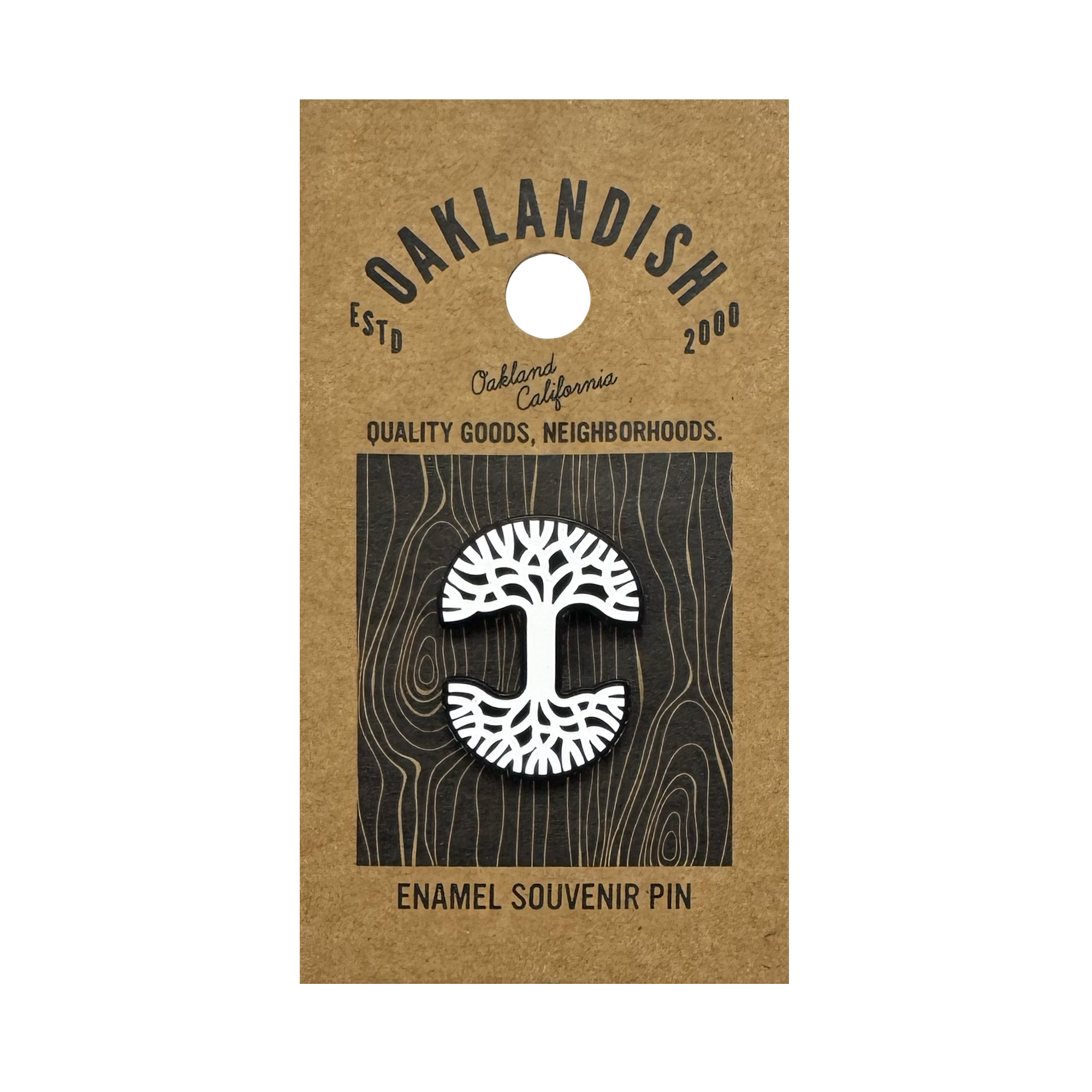 The Oaklandish Logo Enamel Pin by Oaklandish is a white enamel lapel pin shaped like an oak tree, attached to brown kraft paper backing and featuring text: “OAKLANDISH ESTD 2000,” “Oakland California,” and “ENAMEL SOUVENIR PIN.”.