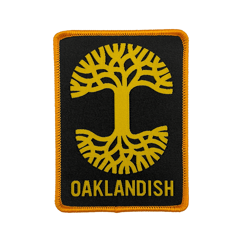 Black woven iron-on patch with gold Oaklandish tree logo and wordmark.