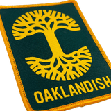 Close-up of forest green woven iron-on patch with gold Oaklandish tree logo and wordmark.