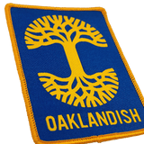 Close-up of royal blue woven iron-on patch with gold Oaklandish tree logo and wordmark.